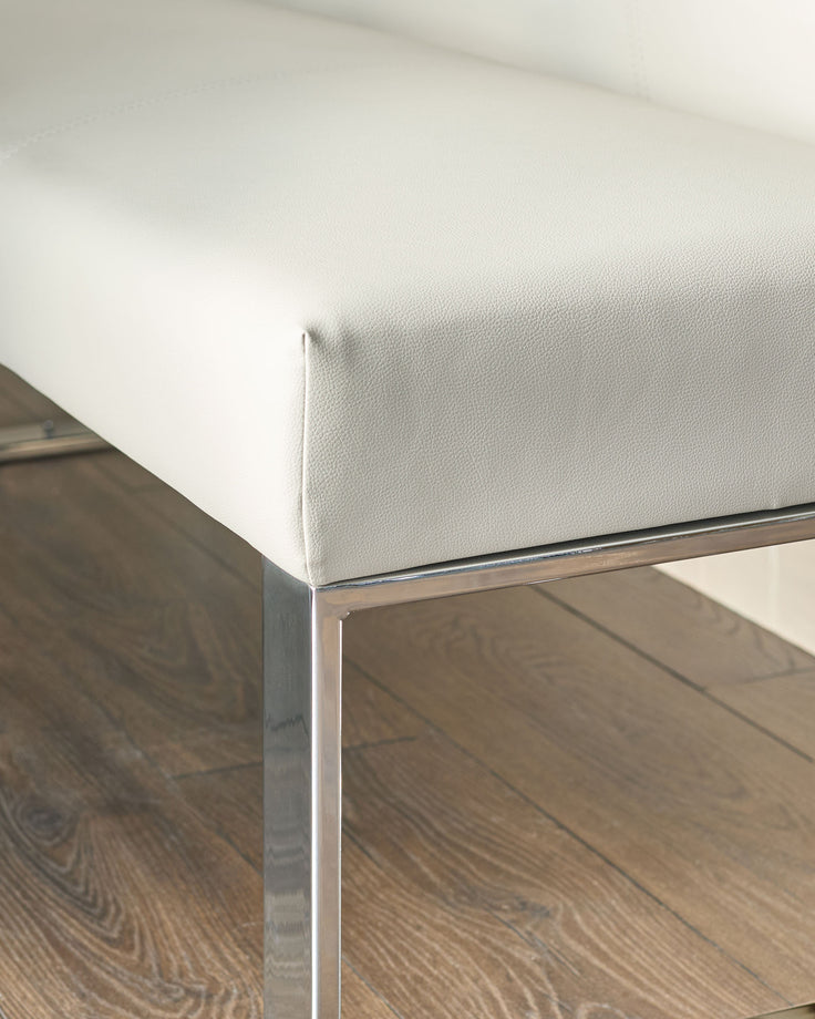 Light grey faux leather corner bench with chrome legs, angled detail shot showing cushioned seat and metal frame.