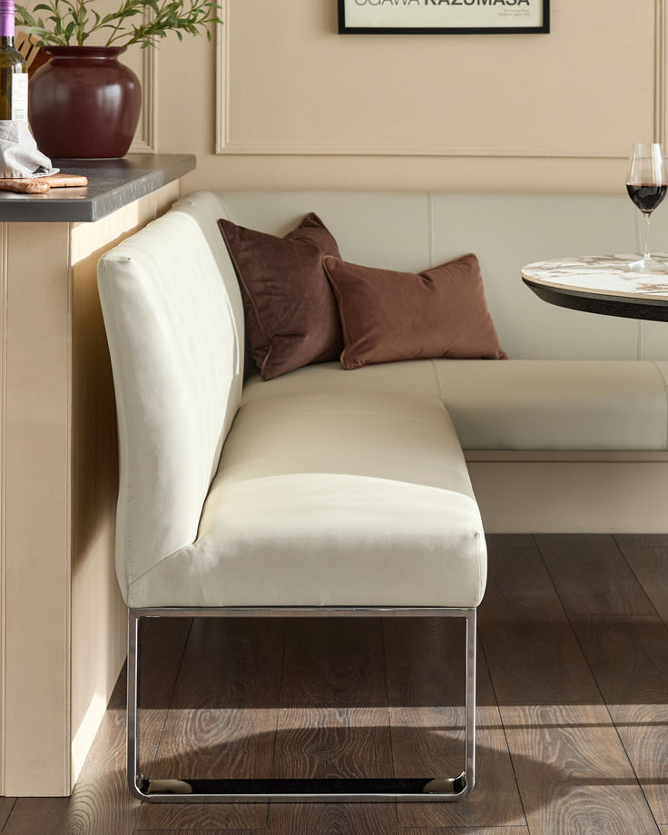 Light grey faux leather dining bench with chrome legs, styled with brown cushions in a contemporary dining room setting.