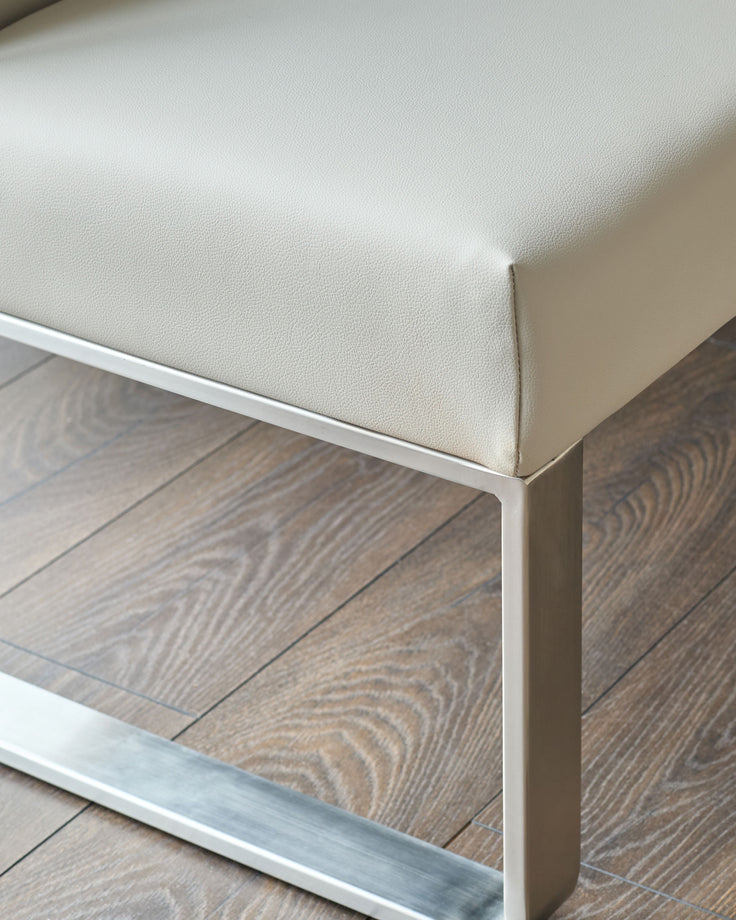 Light grey faux-leather corner bench with stainless steel frame, angled detail view showing seating surface and base.
