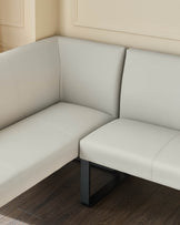 Light grey corner bench seat with black metal legs, positioned against cream walls with dark wood flooring.