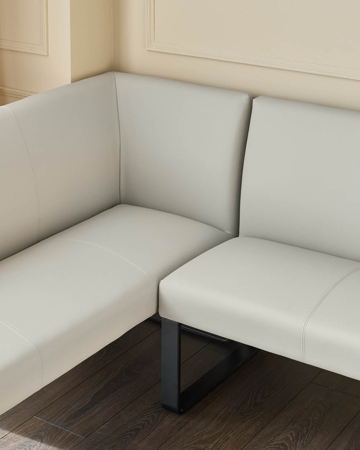 Light grey corner bench seat with black metal legs, positioned against cream walls with dark wood flooring.