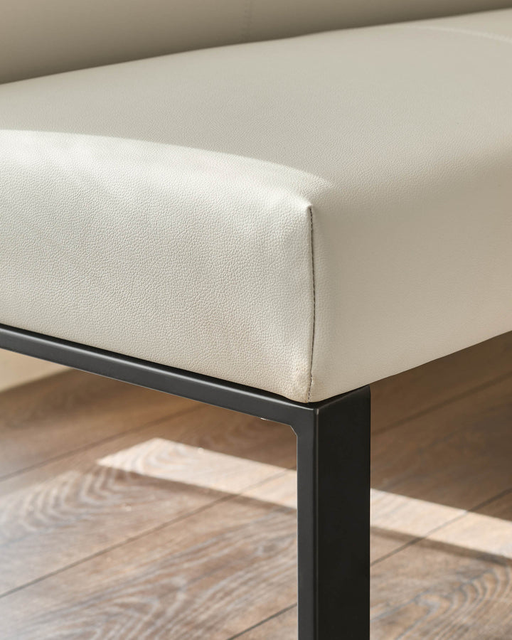 Light grey upholstered corner bench with black metal legs, shown from a side angle on wooden flooring.