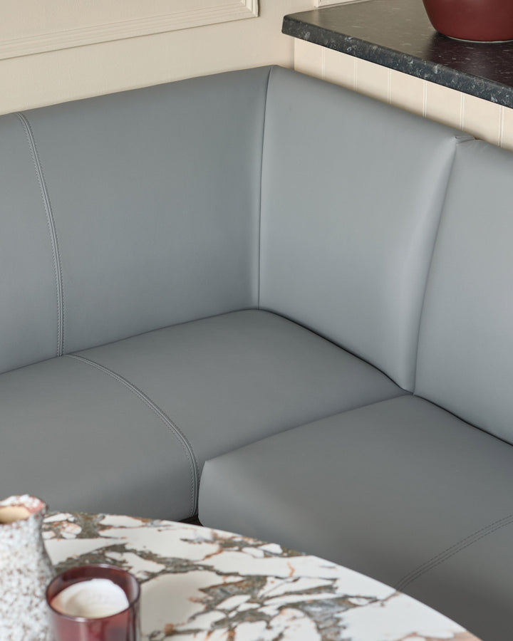 Mid-grey upholstered corner bench with black legs, showing close-up of seat cushions and backrest stitching details.