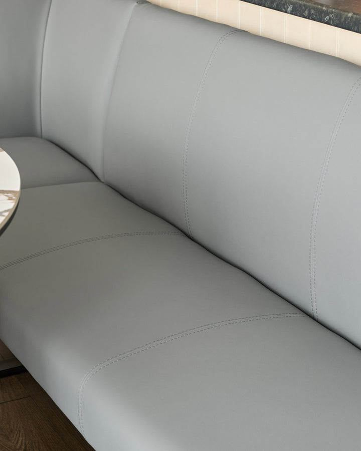 Light grey upholstered corner bench with stitched seams, viewed from side angle showing cushioned seat and backrest.