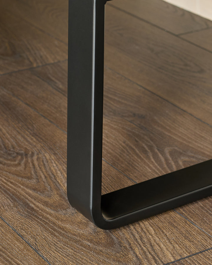 Black metal leg detail of grey corner bench on wooden floor, close-up side view.