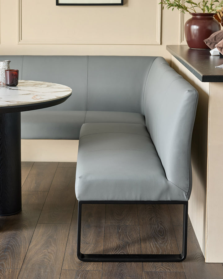 Grey upholstered corner bench with black metal legs, shown in a modern dining setting with round marble table.