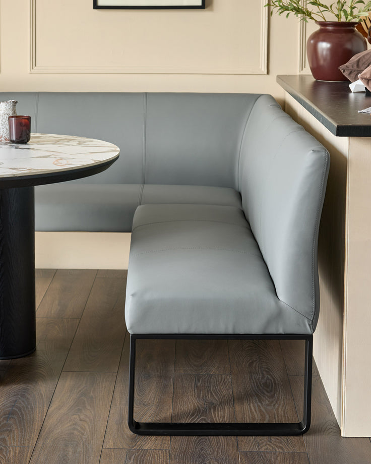 Grey upholstered corner bench with black metal legs, shown in a modern dining setting with round marble table.