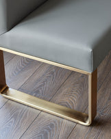 Mid-grey faux leather dining bench with brushed brass leg detail, shown from close-up angle on wooden flooring.