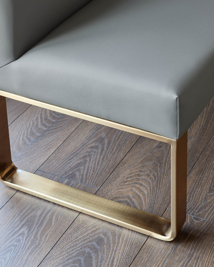 Mid-grey faux leather dining bench with brushed brass leg detail, shown from close-up angle on wooden flooring.