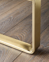 Brushed brass leg detail of dining bench on wood flooring, showing curved metal foot and upholstered base.