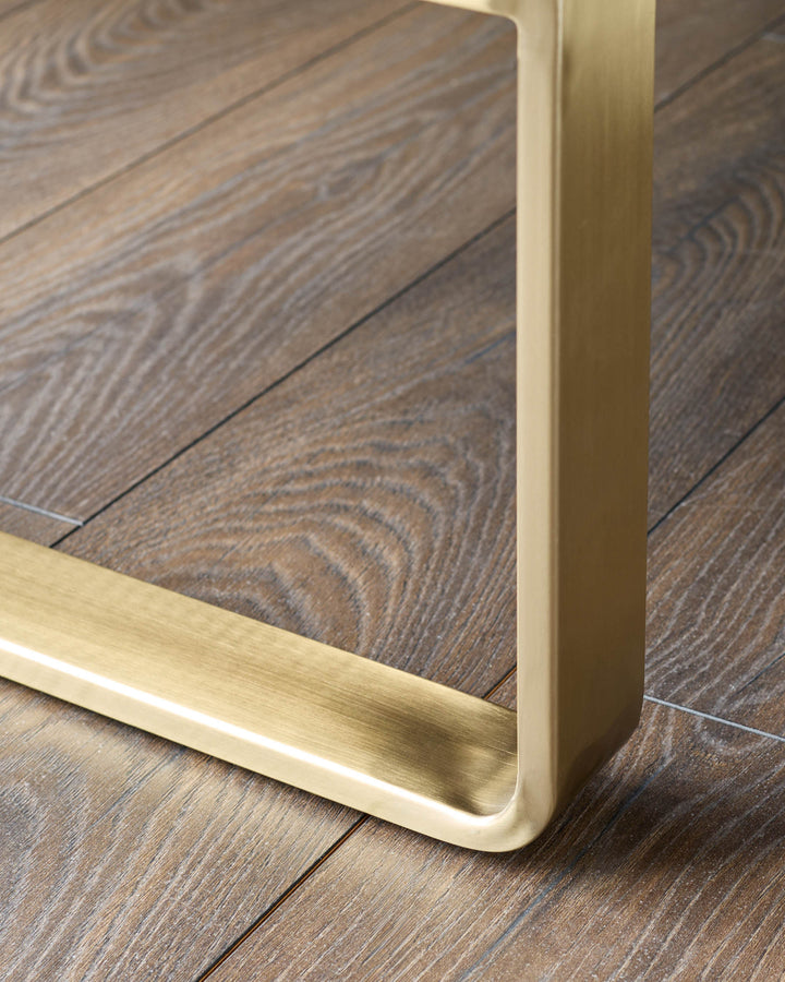 Close-up of brushed brass leg on grey dining bench, showing metal finish detail on wood flooring.