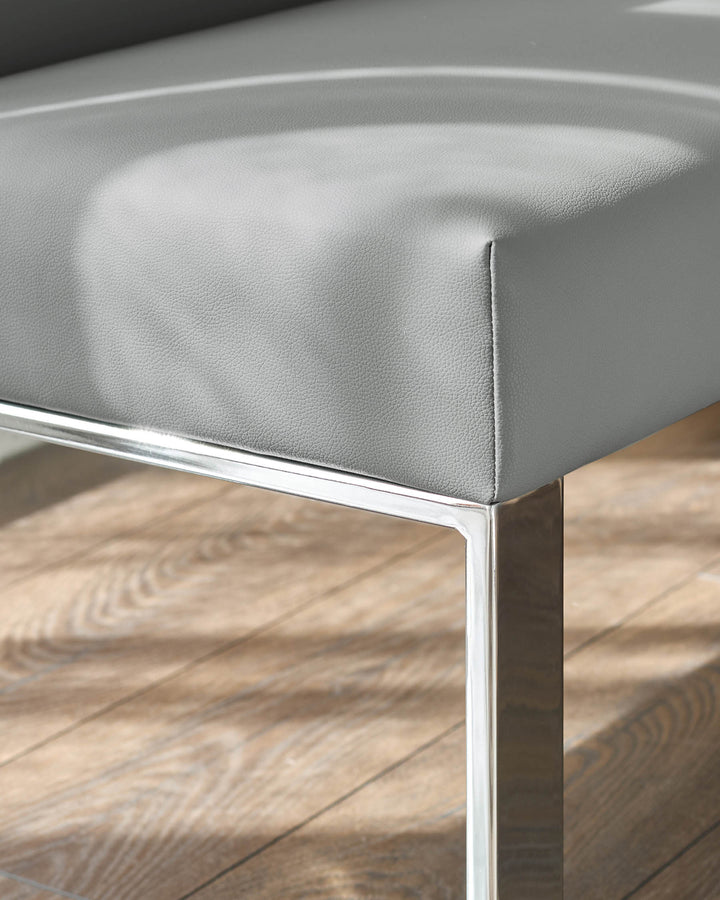 Grey faux-leather dining bench with chrome leg detail, shown at an angle on wooden flooring.
