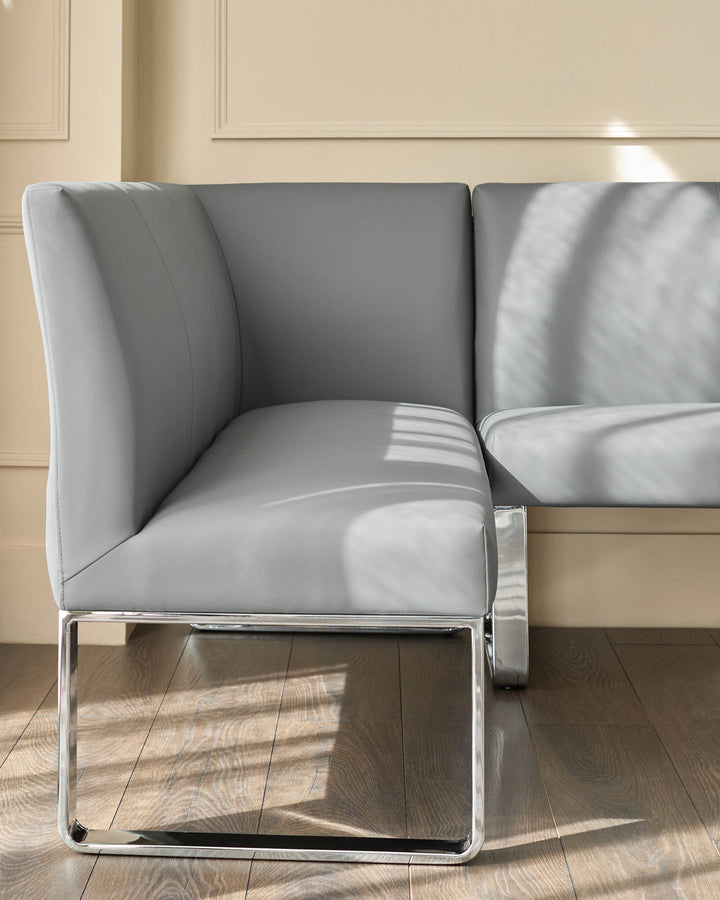Grey faux-leather corner dining bench with chrome legs, shown at an angle in a bright interior space.