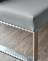 Grey faux-leather corner bench with stainless steel frame, viewed from side angle on wooden flooring.