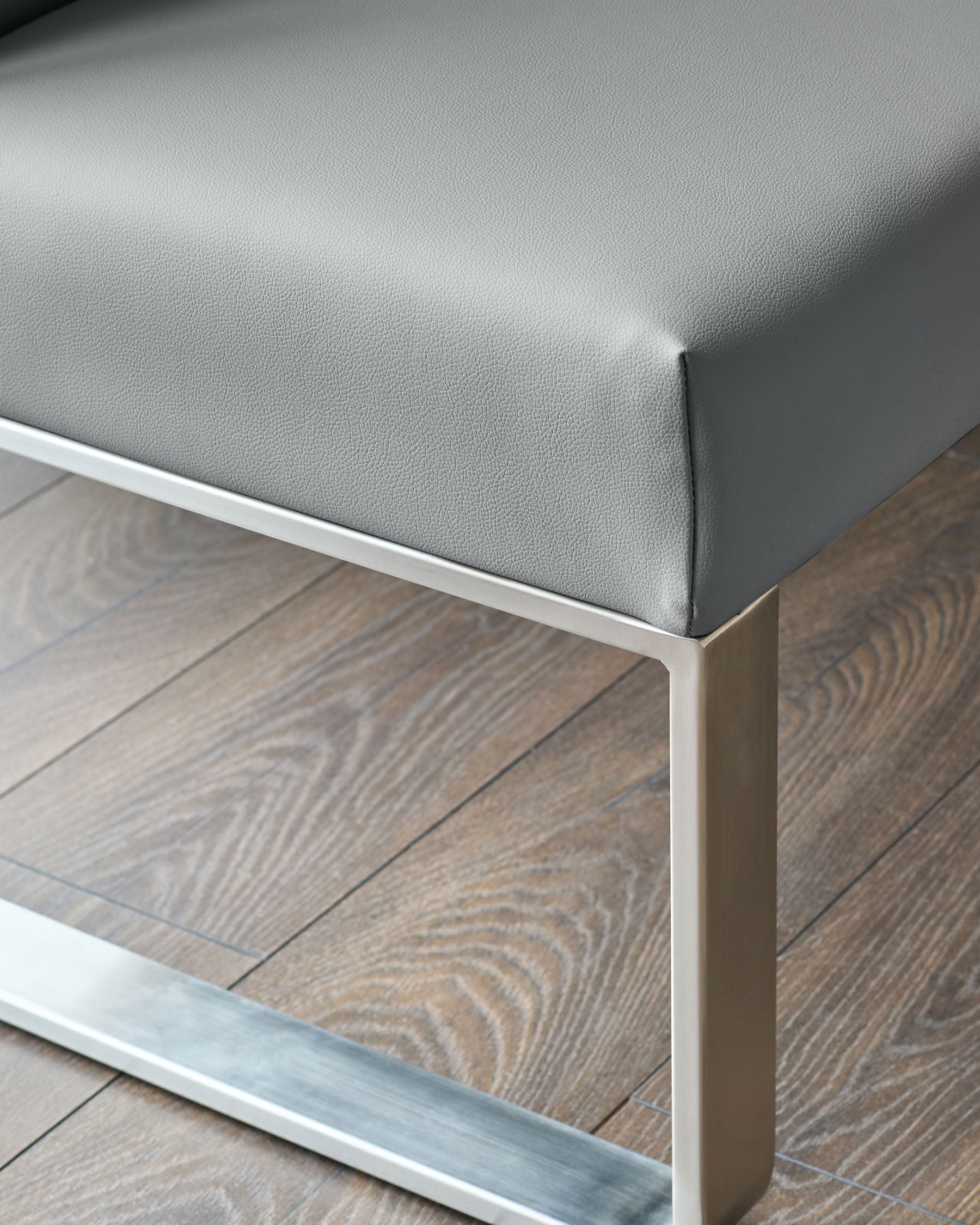 Grey faux-leather corner bench with stainless steel frame, viewed from side angle on wooden flooring.