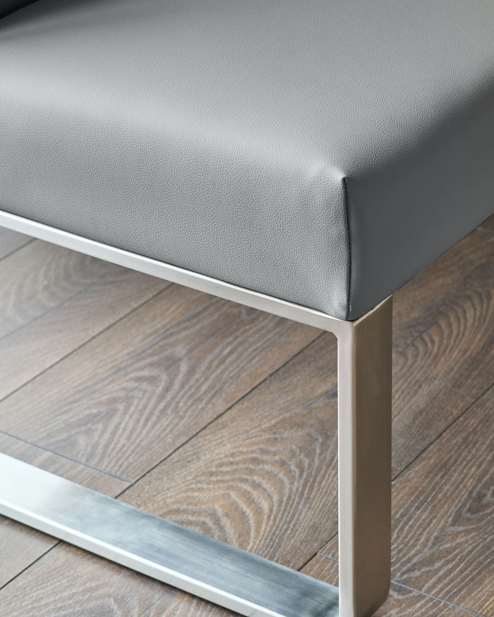 Grey faux-leather corner bench with stainless steel frame and white trim, shown at an angle on wooden flooring.