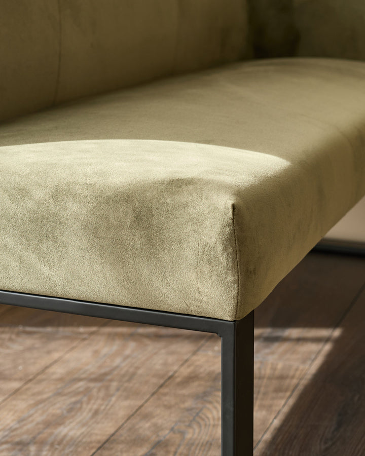 Cream upholstered bench with black metal legs, angled side view showing seat cushion and corner detail on wooden floor.