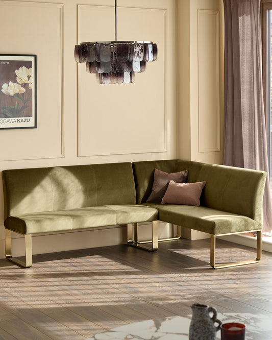 Olive green corner bench with brushed brass legs, styled in a modern living room with pendant light and cream walls.