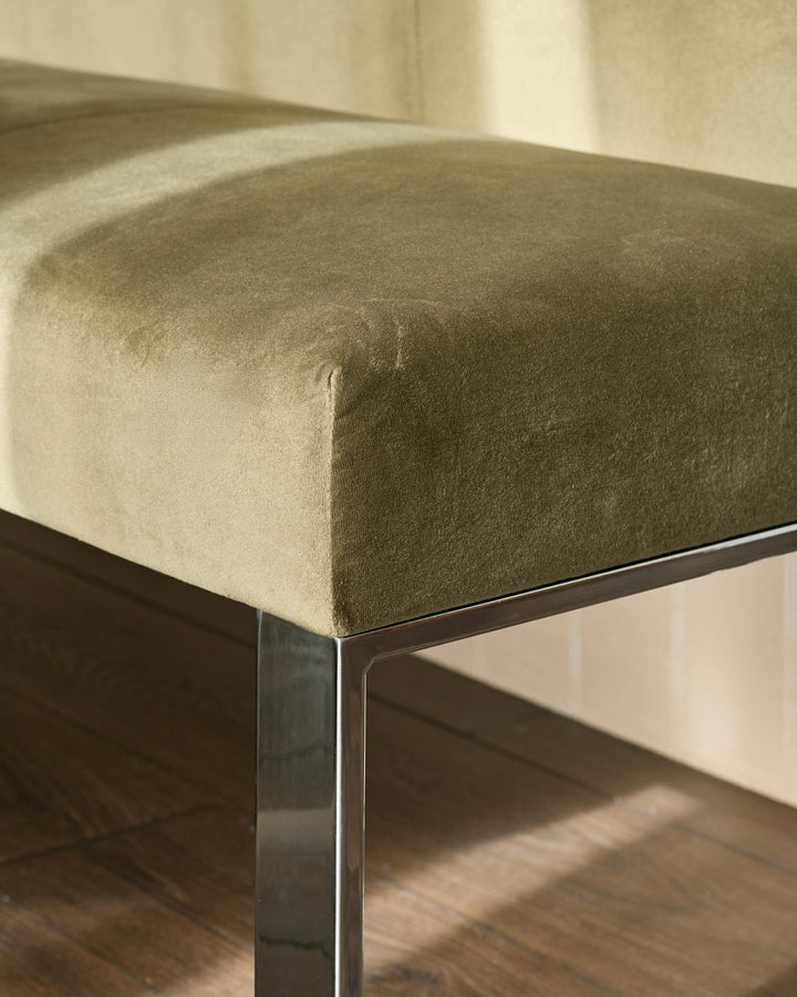 Olive green upholstered corner bench with chrome legs, angled detail shot showing curved seating surface and metal frame.