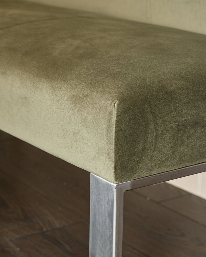 Olive green upholstered bench corner with stainless steel leg, close-up detail shot.