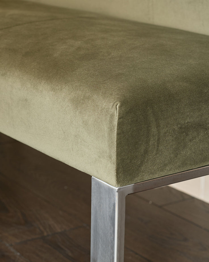 Olive green upholstered bench corner with stainless steel leg, close-up detail shot.