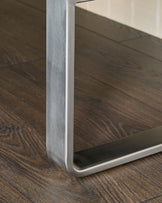 Stainless steel leg detail of Loop bench, showing brushed metal finish and curved base on dark wood floor.