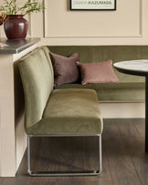 Olive green corner bench with stainless steel legs, styled with mauve pillows in a modern interior setting.