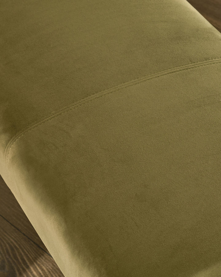 Olive green velvet bench close-up showing curved seam detail and soft upholstered surface texture.