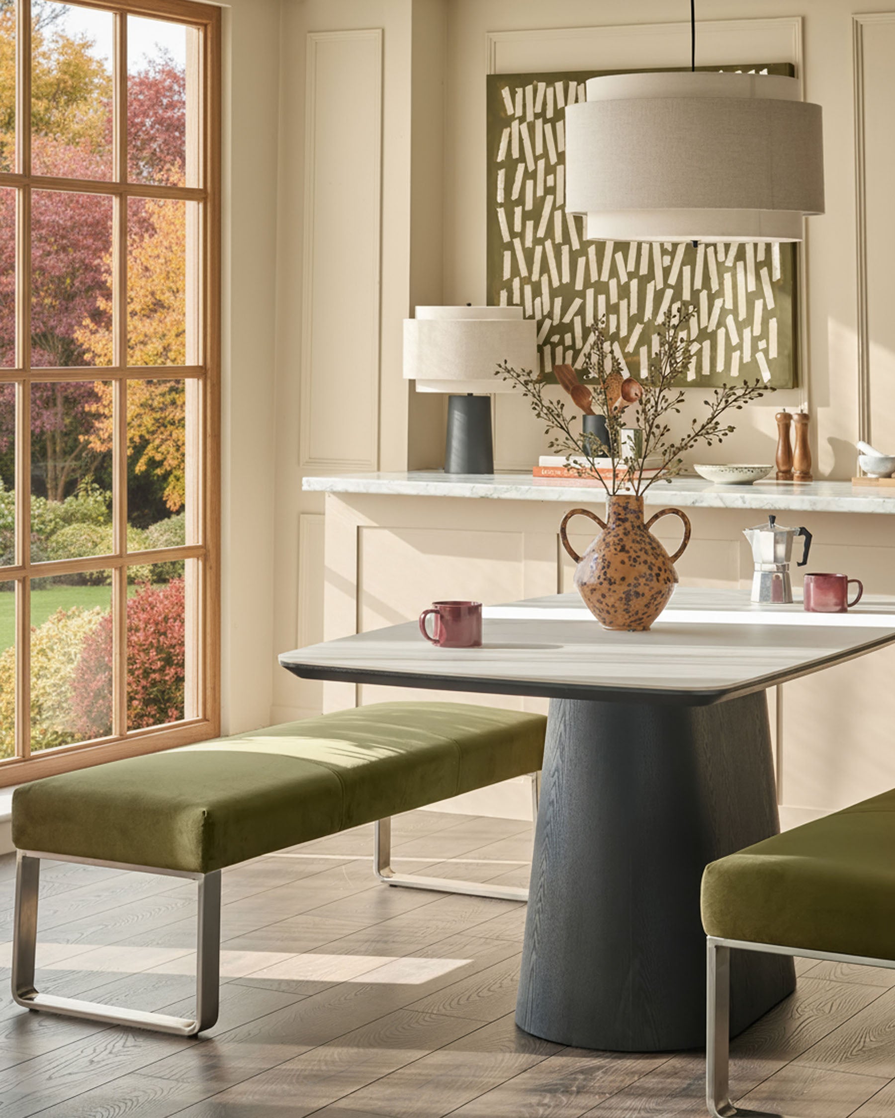 Loop 3-seater velvet bench in olive green with stainless steel legs, positioned at a dining table in a modern interior setting.