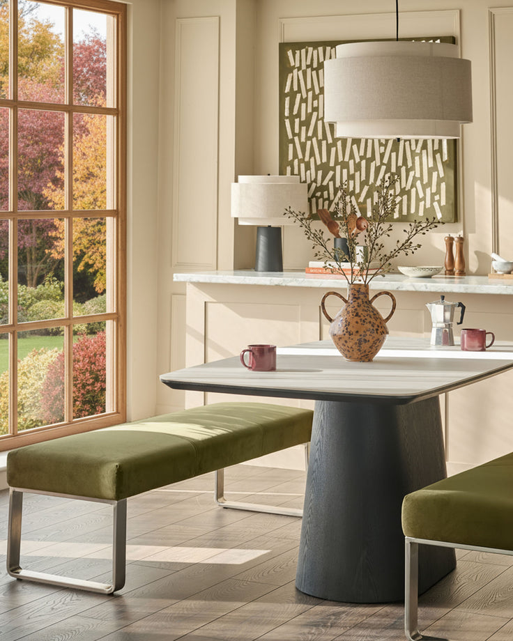 Loop 3-seater velvet bench in olive green with stainless steel legs, positioned at a dining table in a modern interior setting.