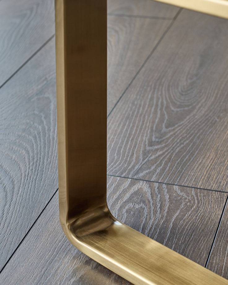 Brushed brass leg detail of olive green velvet bench, angled view on Grey wood flooring.