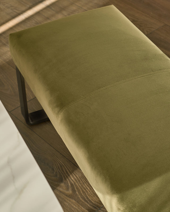Olive green velvet bench with black metal legs, angled top view showing cushioned seat surface and seam detail.