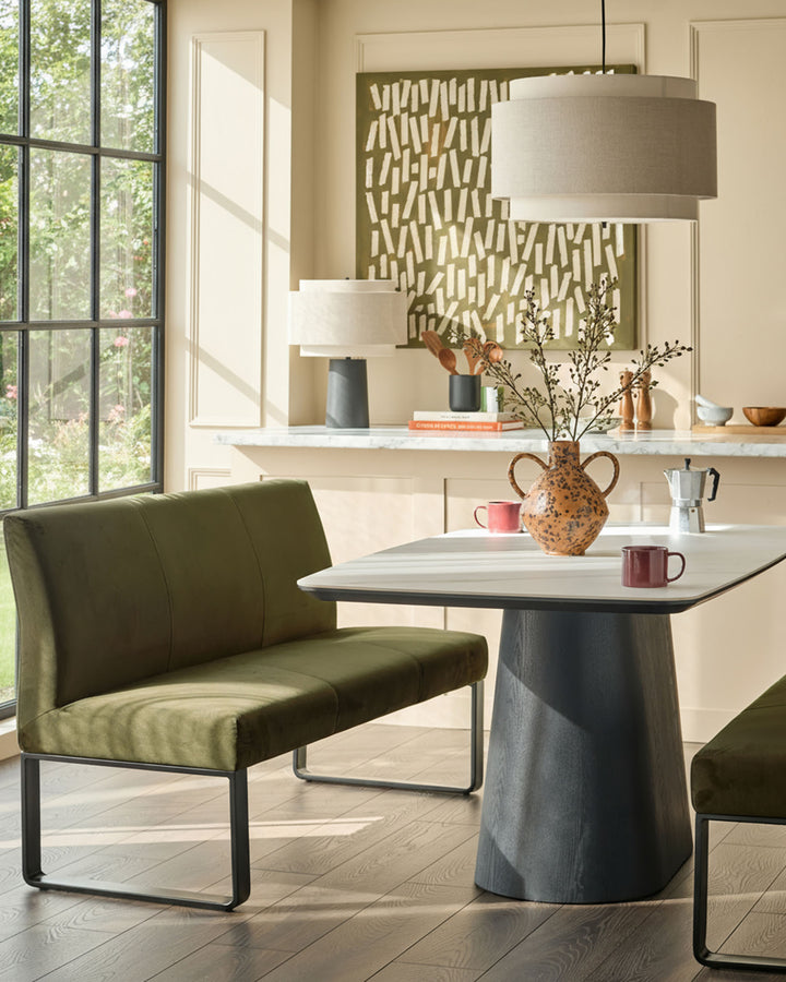 Olive green velvet bench with backrest and black metal frame, shown in modern dining room setting.