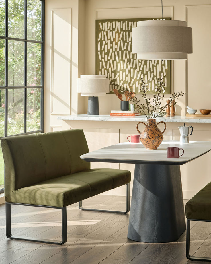 Olive green velvet bench with backrest and black metal frame, shown in modern dining room setting.