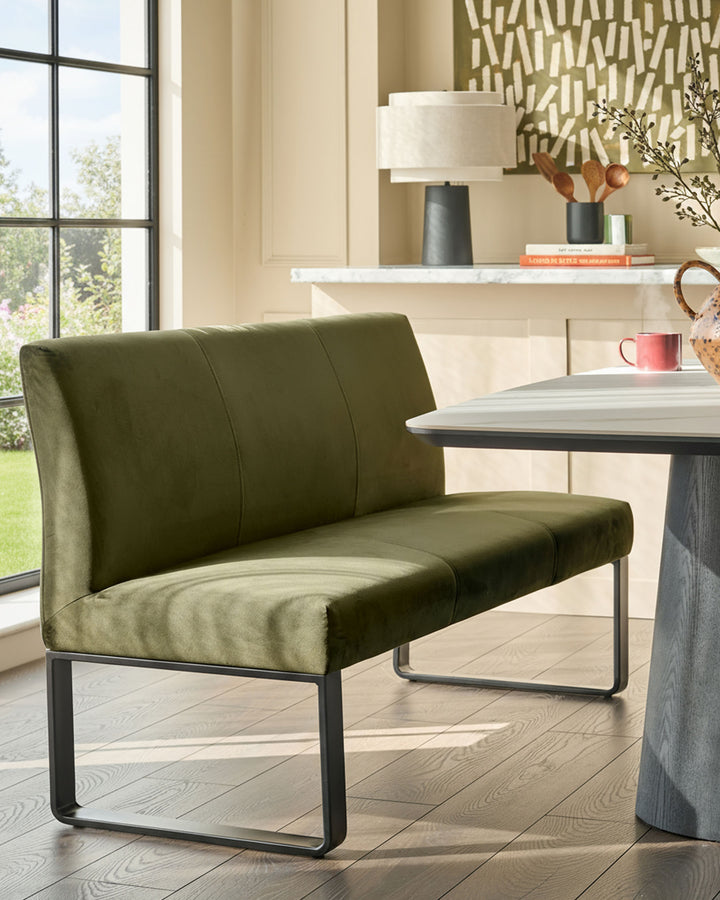 Loop 3-seater velvet bench with backrest in olive green, black metal frame, shown in contemporary dining setting.