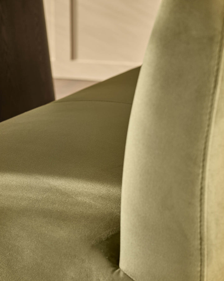 Olive green velvet bench with curved backrest and stainless steel leg, close-up detail view.