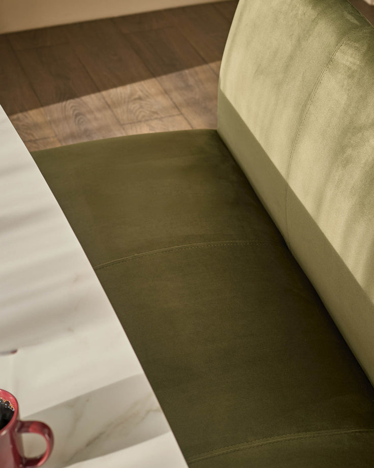 Olive green velvet bench with backrest, angled view showing seating surface and wooden floor detail.