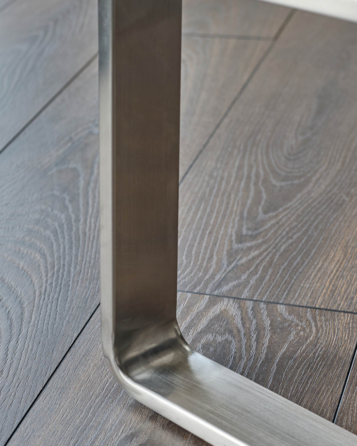 Stainless steel leg detail of olive green velvet bench, showing brushed metal finish and wood flooring.