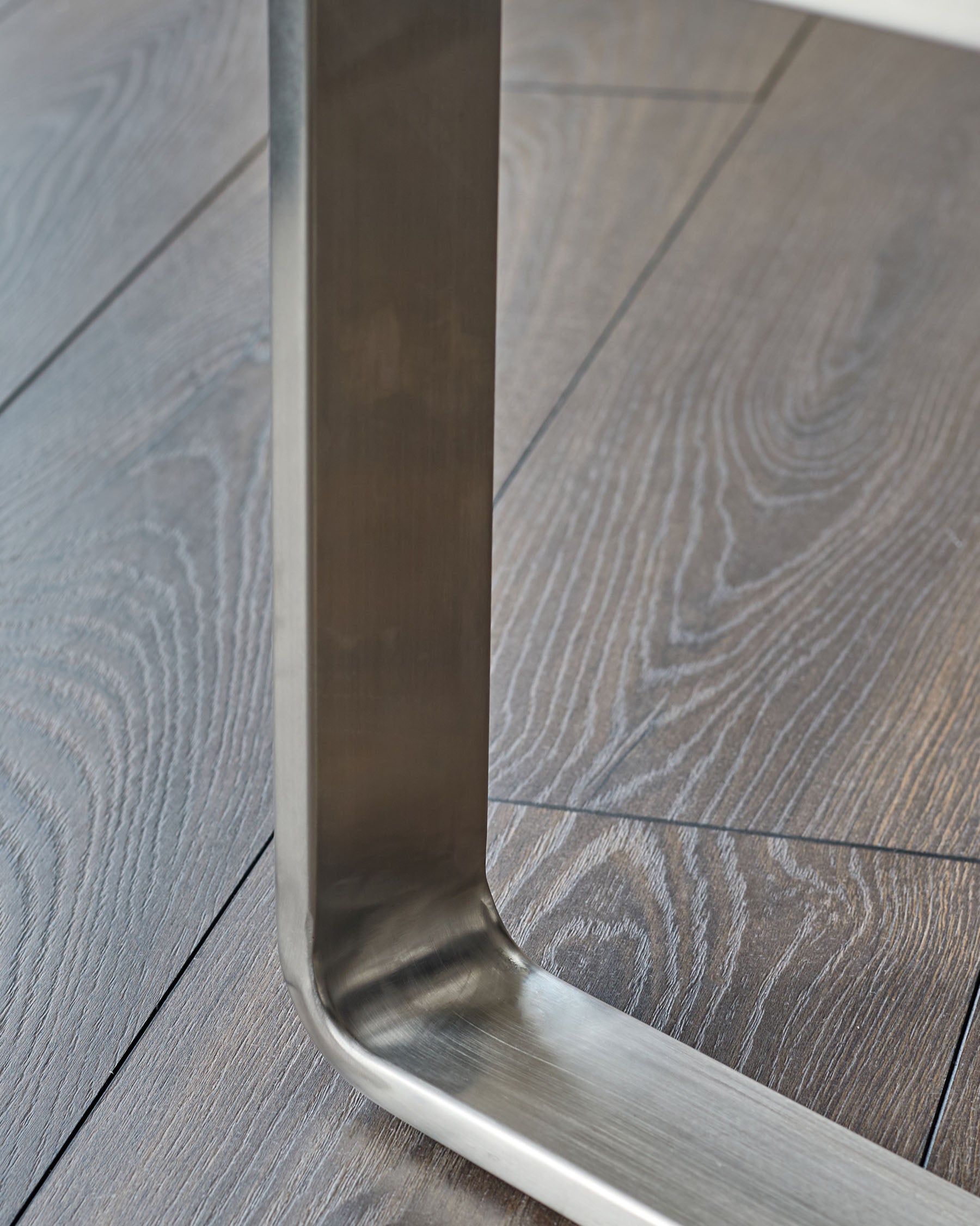 Stainless steel loop handle on modern bench with grey wood-grain upholstery, close-up detail view.