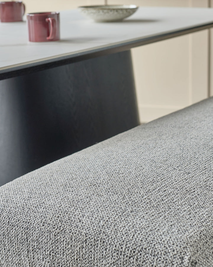 Grey fabric 3-seater bench with black metal frame, shown from low angle highlighting the textured upholstery and sleek base.