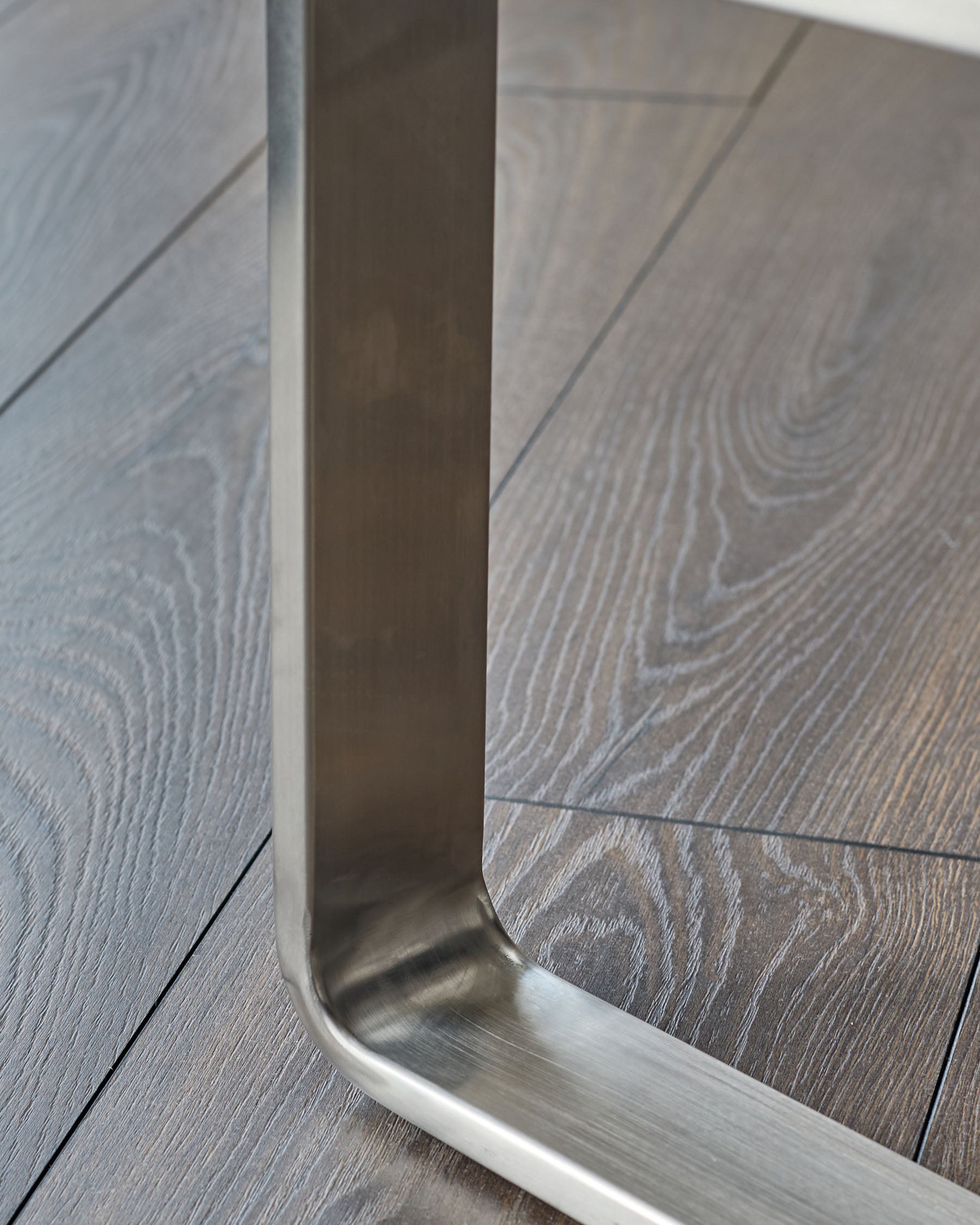 Stainless steel loop handle detail on Grey upholstered bench with wooden floor background.