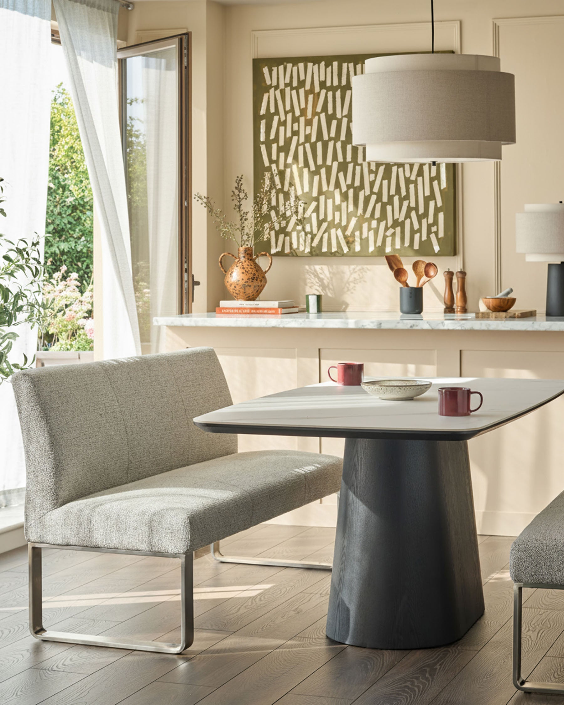 Grey fabric 3-seater bench with backrest and stainless steel frame, shown in modern dining setting.