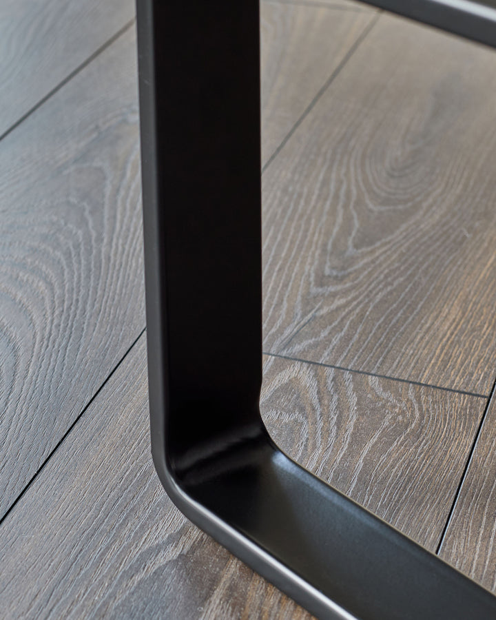 Black metal frame detail of grey fabric bench, showing curved base and wood-look flooring.