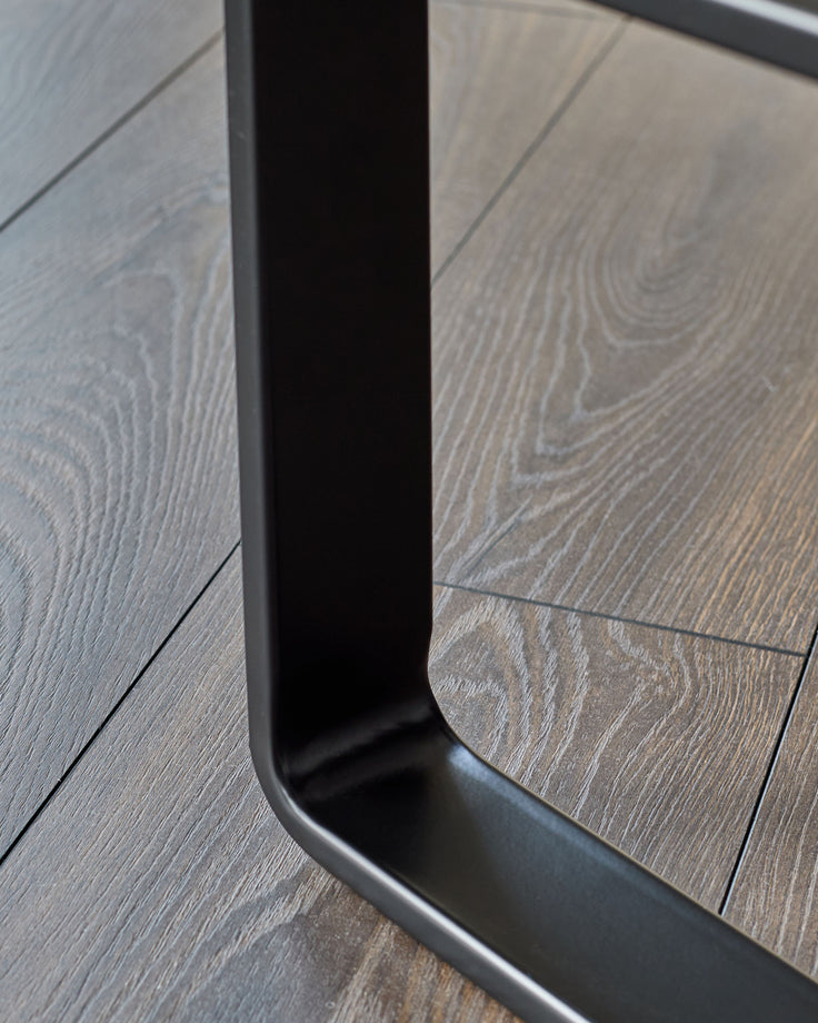 Black metal frame detail of grey fabric bench, showing curved base and wood-look flooring.