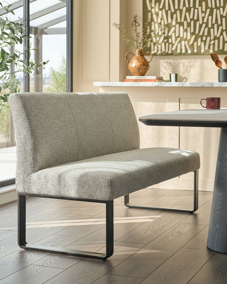 Grey fabric bench with backrest and black metal frame, positioned in a bright modern interior space.