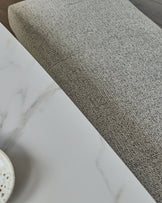 Grey fabric 3-seater bench without backrest, shown at an angle displaying the textured upholstery and brushed brass base.