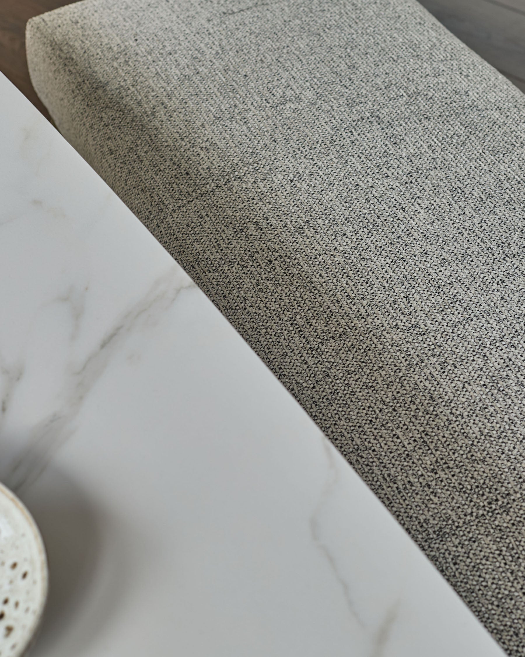 Grey fabric 3-seater bench without backrest, shown at an angle displaying the textured upholstery and brushed brass base.