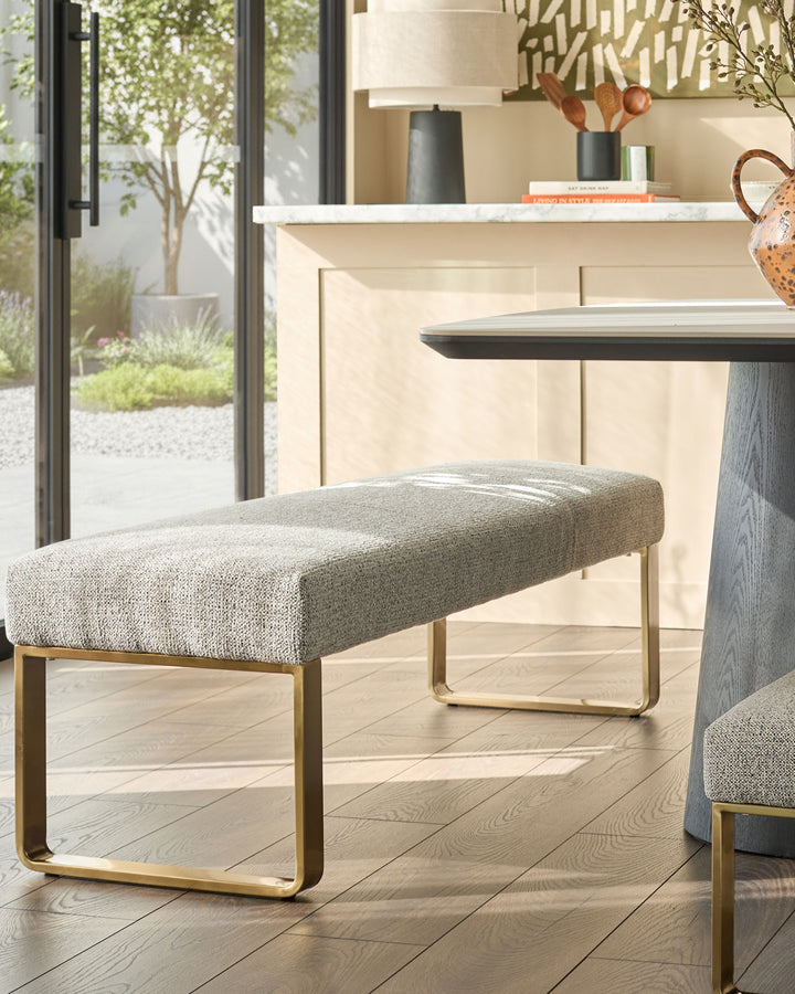 Loop 3-seater fabric bench without backrest in grey with brushed brass legs, shown in a modern living room setting.