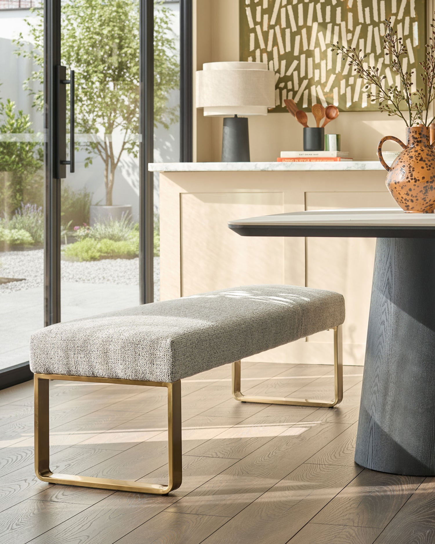 Loop 3-seater fabric bench without backrest in grey with brushed brass frame, styled in modern interior.