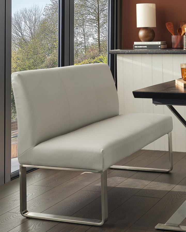 A light grey leather dining bench with a brushed metal frame, set in a modern dining room.